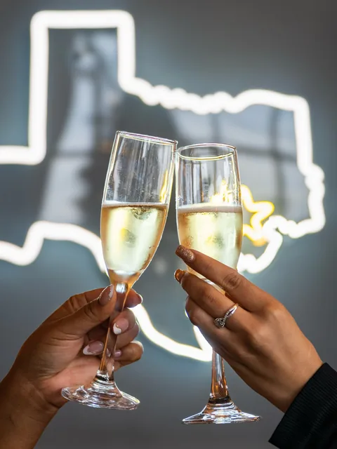 Champagne toast in front of the neon Texas at Chapman & Kirby